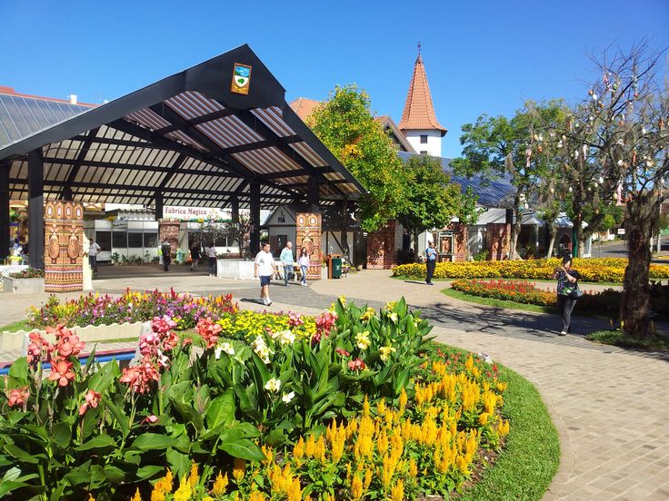 Praça central de Nova Petrópolis com flores coloridas, arquitetura alpina e torre ao fundo